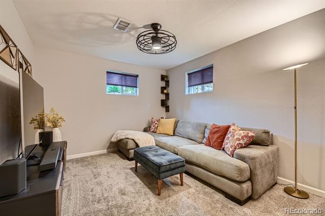 Basement living room with a beige sectional, dark ottoman, and two high windows.
