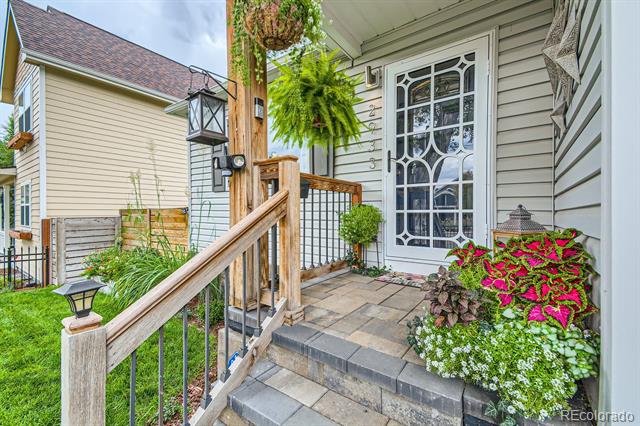 Front entrance with a decorative glass door, wooden railing, hanging ferns, and colorful flowers.