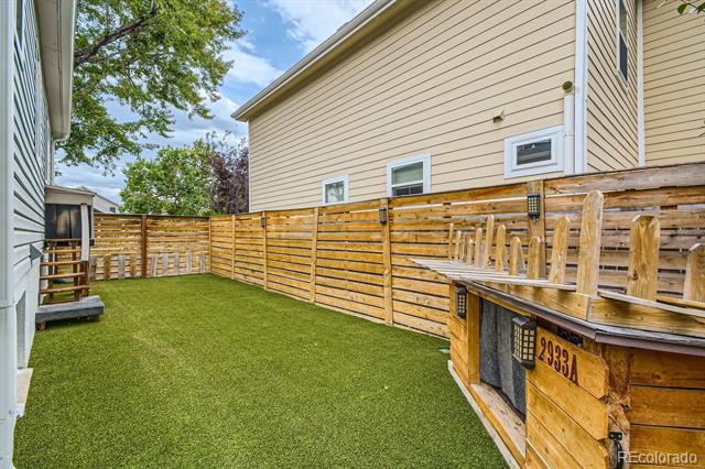 Fenced backyard with artificial turf and a raised wooden deck along one side.