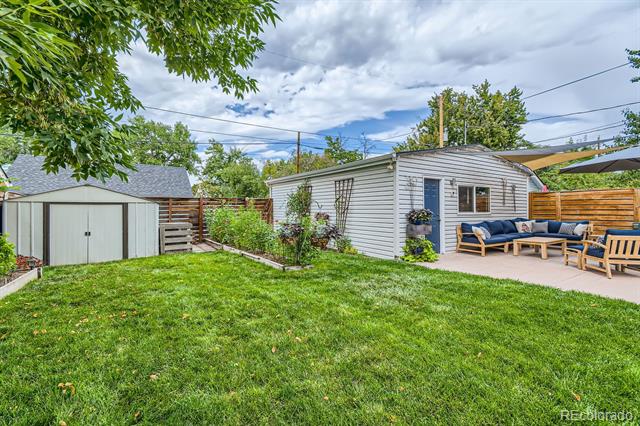 Backyard with a broad lawn, detached shed, and patio seating beside the house.
