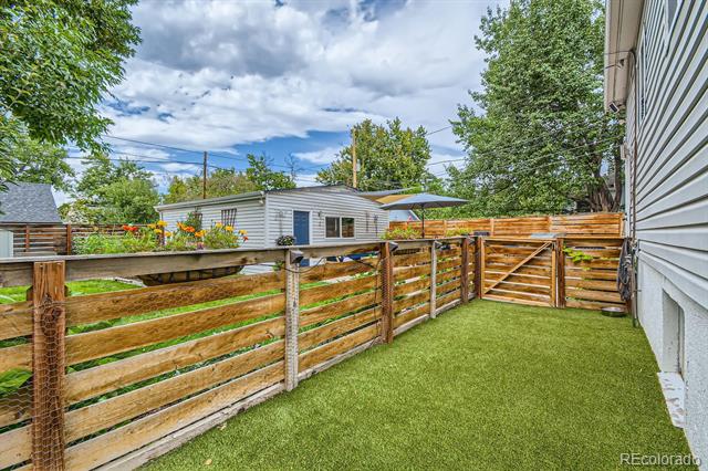 Fenced backyard with artificial turf, a wooden gate, and a covered patio.