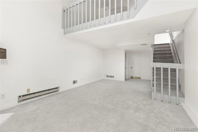 Empty carpeted living area with a staircase and upper-level landing.