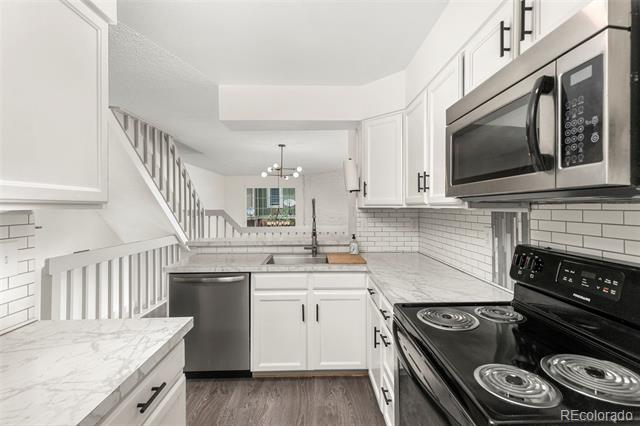White kitchen with marble-look counters, stainless appliances, and a staircase behind it.