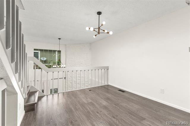 Vacant upstairs landing with gray wood flooring, white stair railings, and a modern chandelier.