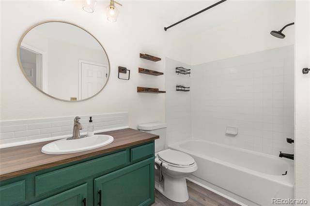 Bathroom with a green wood-topped vanity, round mirror, and white tub and shower.