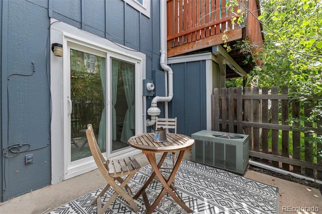Furnished patio with a round wooden table, patterned rug, and sliding glass door beneath a balcony.