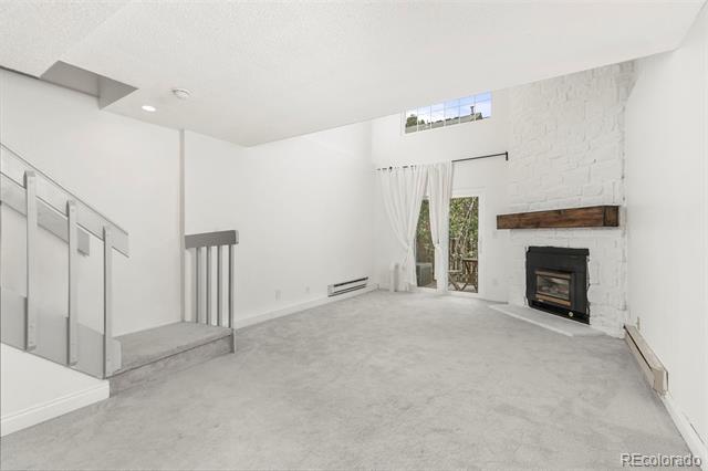 Vacant living room with a white brick fireplace, high ceiling, and glass patio door.