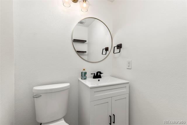 White bathroom with a toilet, vanity, black faucet and hardware, and round mirror.