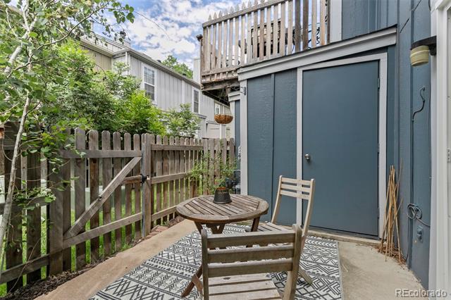 Fenced patio with a wooden table and chairs beside blue siding, beneath an upper balcony.