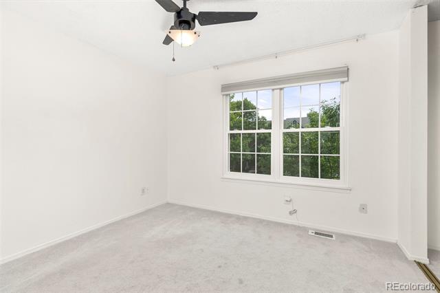 Empty bedroom with light carpet, a black ceiling fan, and a double window overlooking greenery.