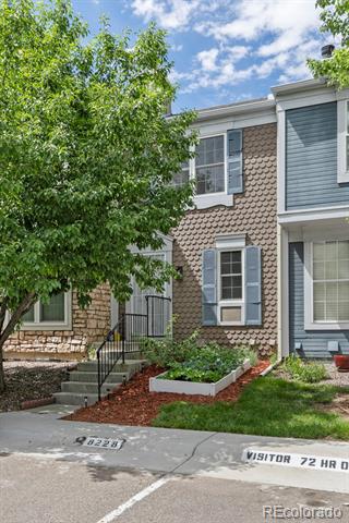 Townhouse exterior with blue-gray trim, front steps, a leafy tree, and a raised flower bed.