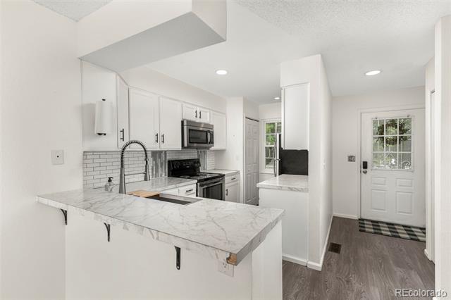 White kitchen with marble-look counters, subway tile backsplash, and a peninsula sink.