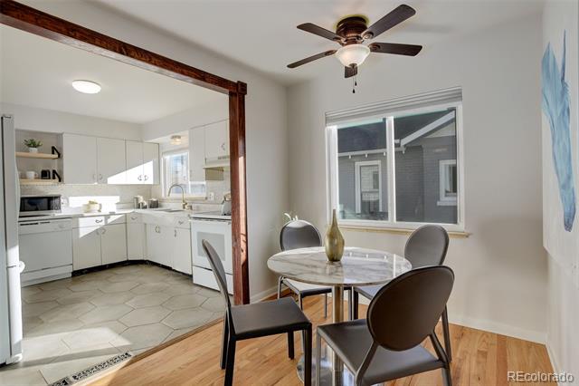 Dining area with a round table and ceiling fan beside a bright white kitchen.