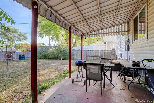 Covered patio with outdoor dining furniture and grill beside a fenced backyard