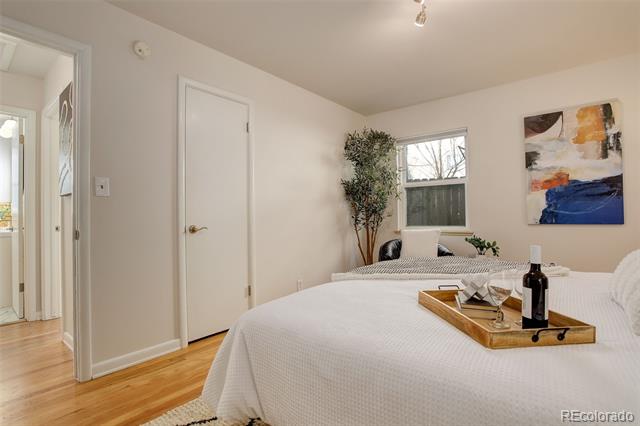 Staged bedroom with a white bed, hardwood floors, and colorful abstract wall art.