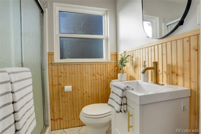 Bathroom with wood wainscoting, a white vanity, glass shower, and toilet.