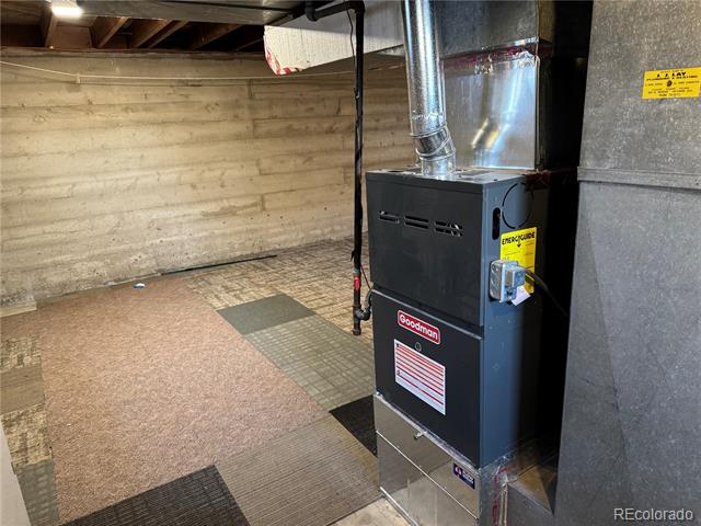 Basement utility area with a Goodman furnace, exposed foundation walls, and tiled flooring.