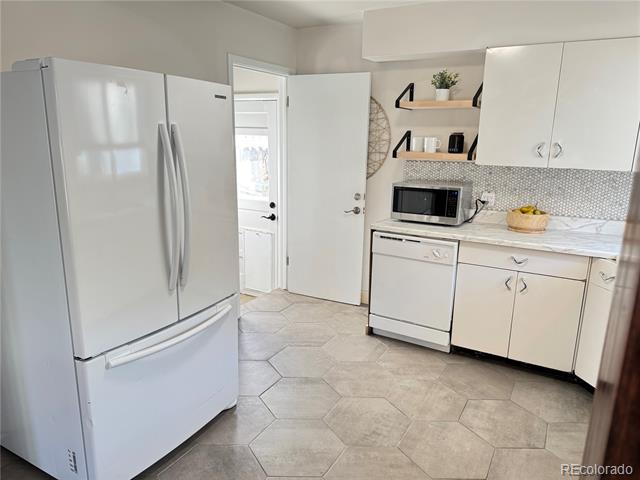 Kitchen with white cabinets, French-door refrigerator, open shelving, and hexagonal tile floor.
