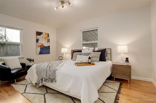 Staged bedroom with white bedding, hardwood floors, a geometric rug, and a black accent chair.