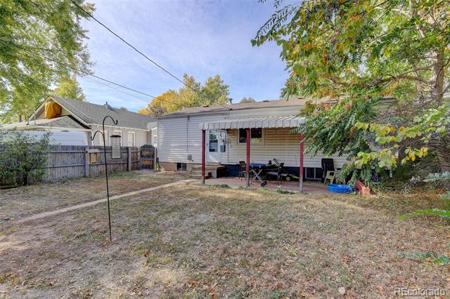 Backyard with a covered patio and seating, a fenced lawn, and mature autumn trees.