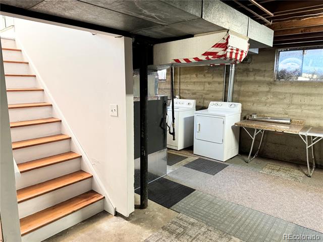 Basement laundry area with washer and dryer beside stairs and a utility sink.
