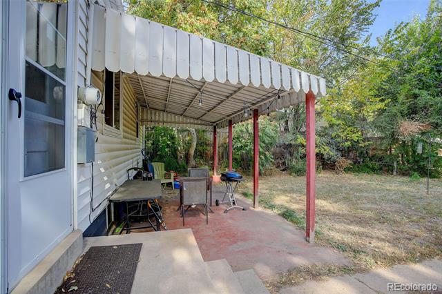 Covered patio with red posts beside a white-sided house, overlooking a tree-lined yard.