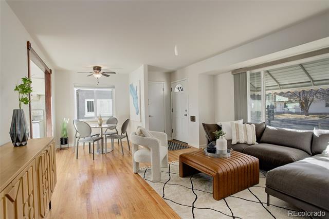 Living room with a gray sectional and large windows, open to a dining area with hardwood floors.