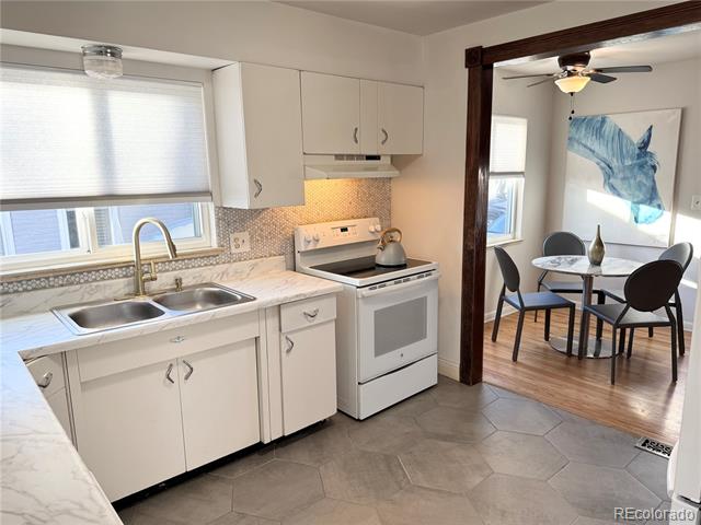 White kitchen with double sink and range, opening to a dining area with blue wall art.