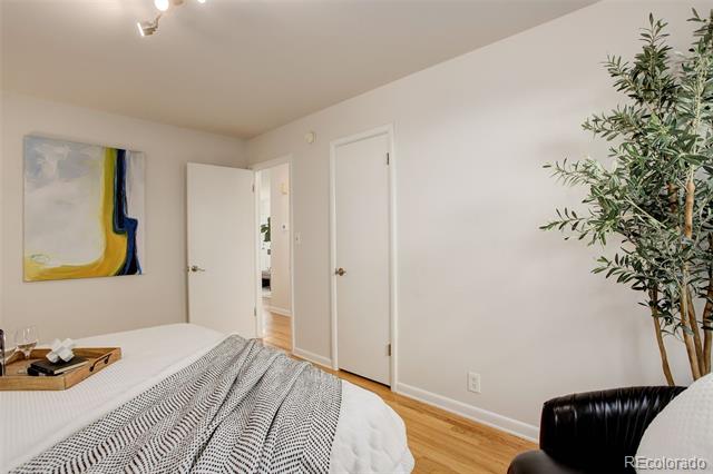 Bedroom with a white bed, patterned blanket, abstract art, and light hardwood floors.