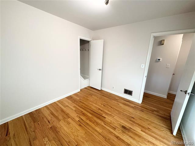 Vacant bedroom with hardwood floors, an open closet, and a doorway to the hall.