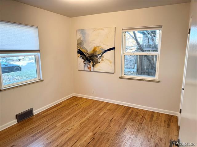 Empty room with hardwood floors, two windows, and an abstract painting.