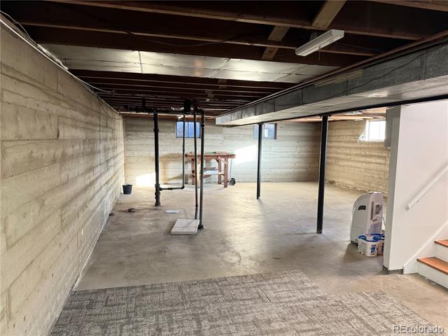 Unfinished basement with exposed joists, concrete walls, and support posts.