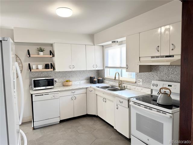 Kitchen with white cabinets, gray mosaic backsplash, and a corner sink beneath a window.