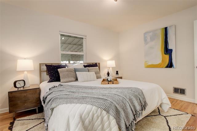 Staged bedroom with a large white bed, patterned bedding, abstract wall art, and hardwood floors.