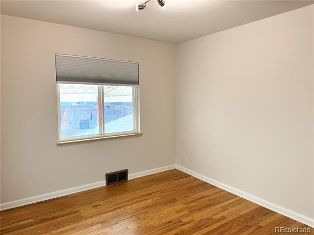 Empty room with polished hardwood floors and a window with a gray roller shade.
