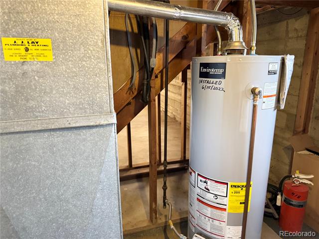 Basement water heater beside a large furnace, with exposed framing and vent pipes.