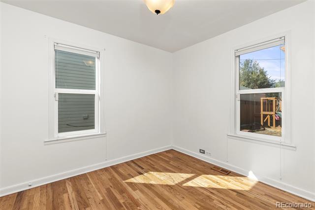 Vacant room with hardwood floors, white walls, and two windows.