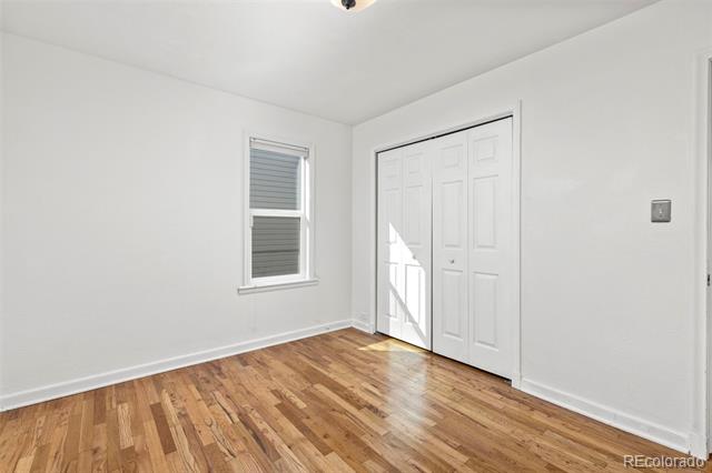 Empty room with hardwood floors, a window with blinds, and double closet doors.