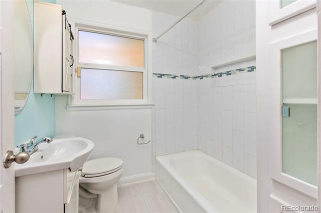 Bathroom with a white bathtub, tiled walls, pedestal sink, toilet, and frosted window.