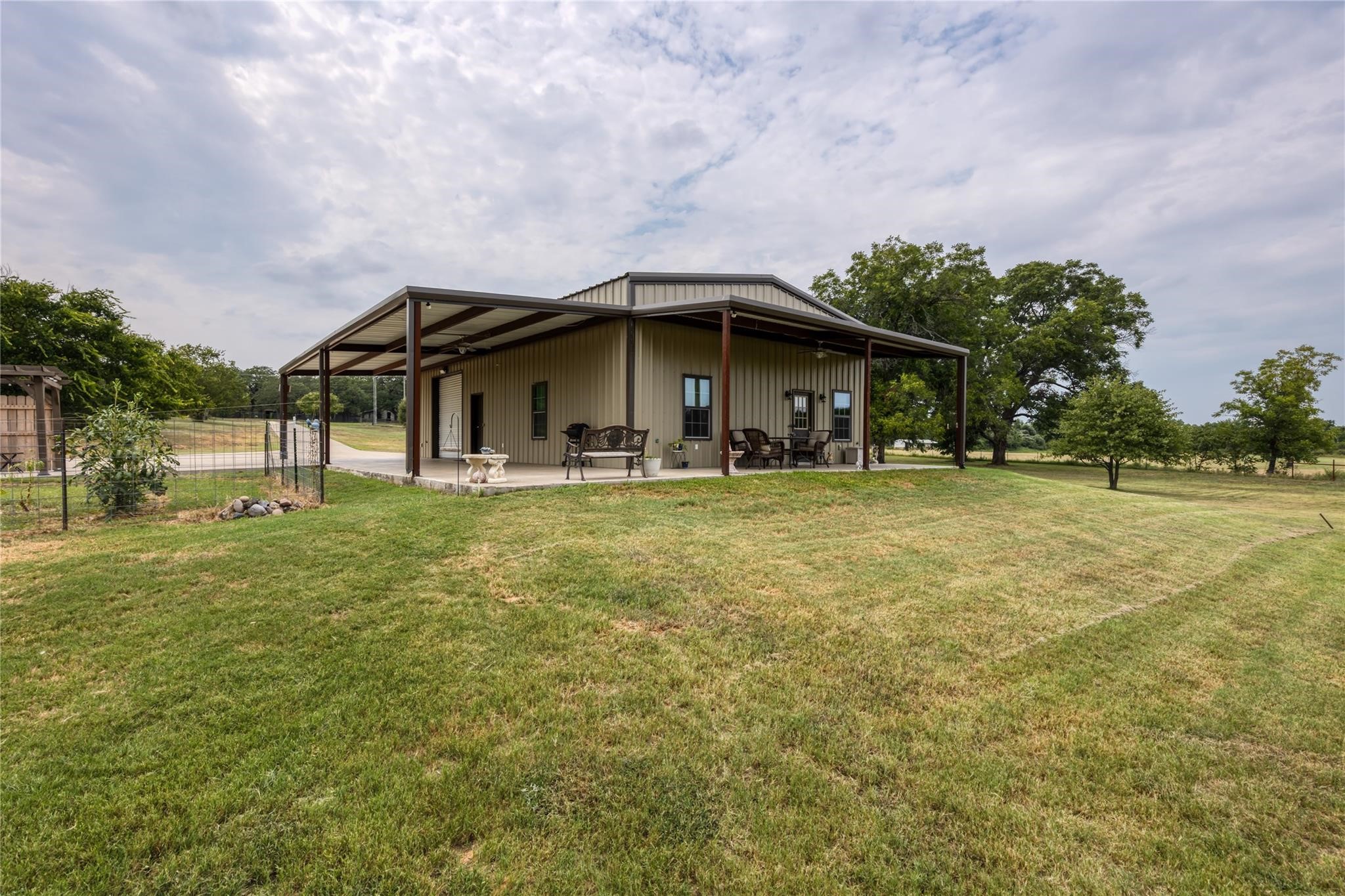 Tan metal-sided home with a large covered porch on a spacious grassy lot.