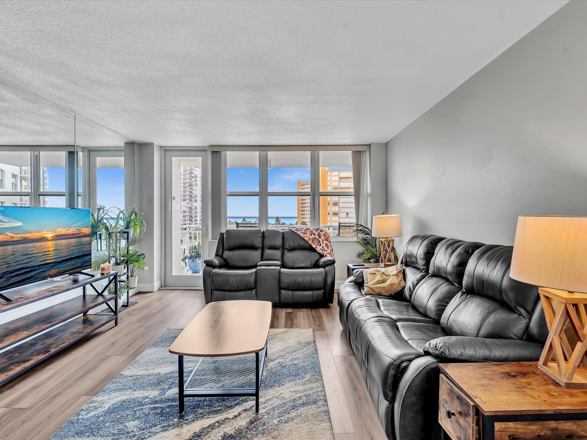Living room with black leather sofas and ocean glimpses through wide windows.
