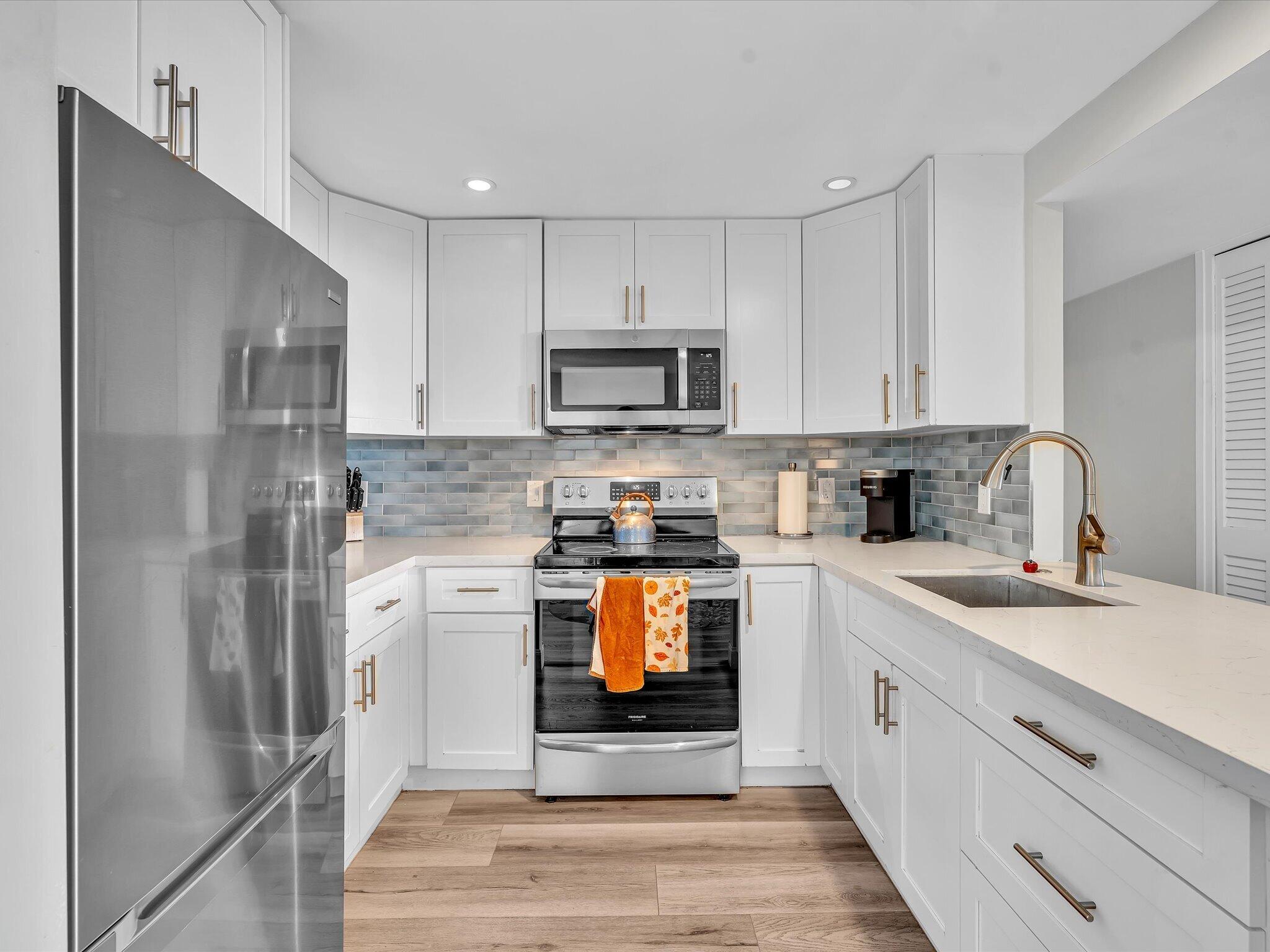 Kitchen with white cabinets, gray-blue tile backsplash, stainless appliances, and a wide sink peninsula.