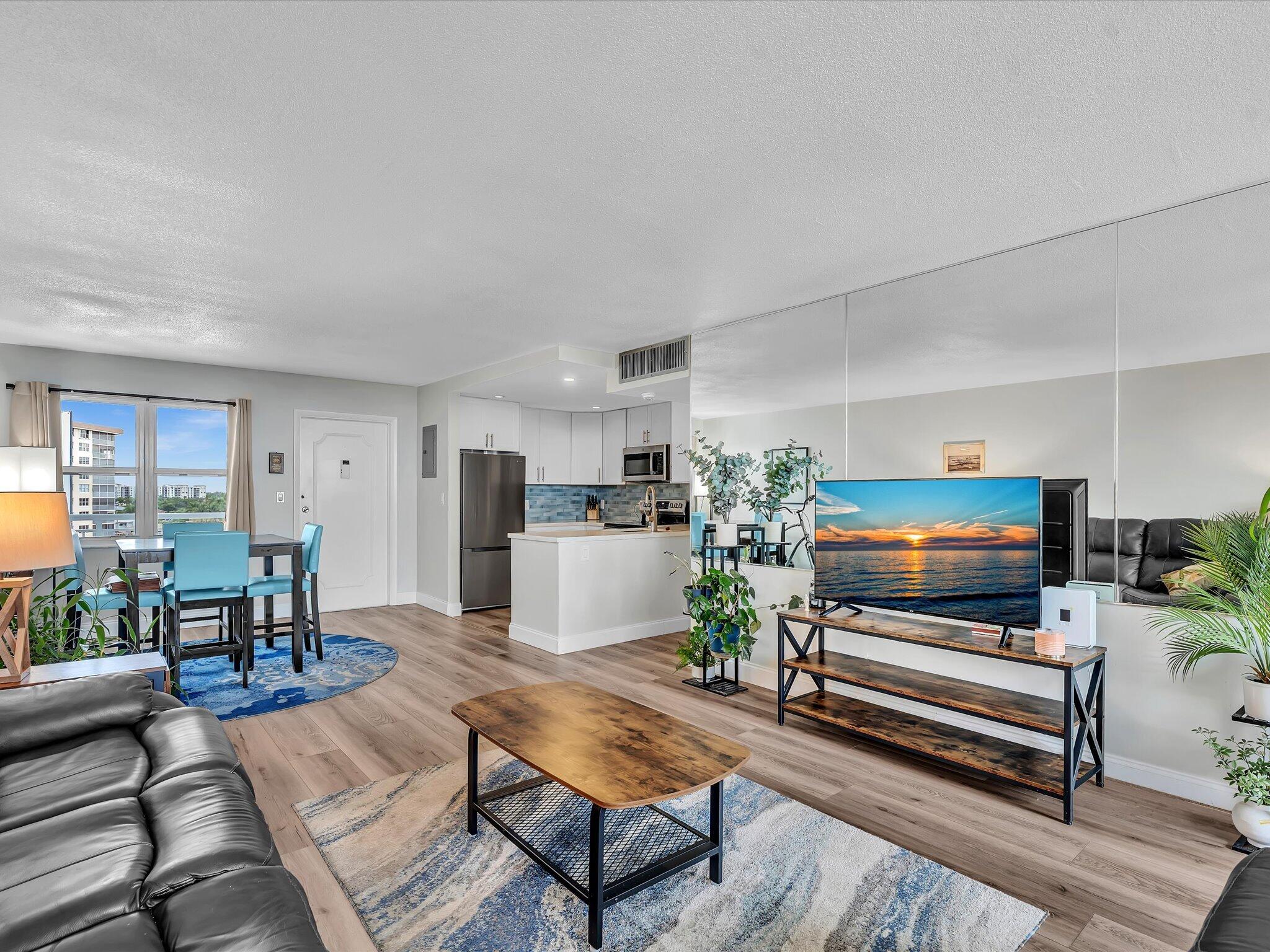 Open-plan living room with mirrored wall, gray leather sofa, and dining area beside windows overlooking water.