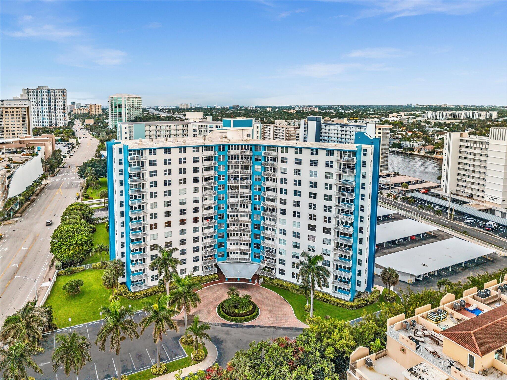 White and turquoise high-rise condominium with balconies, palm-lined grounds, and a circular driveway.