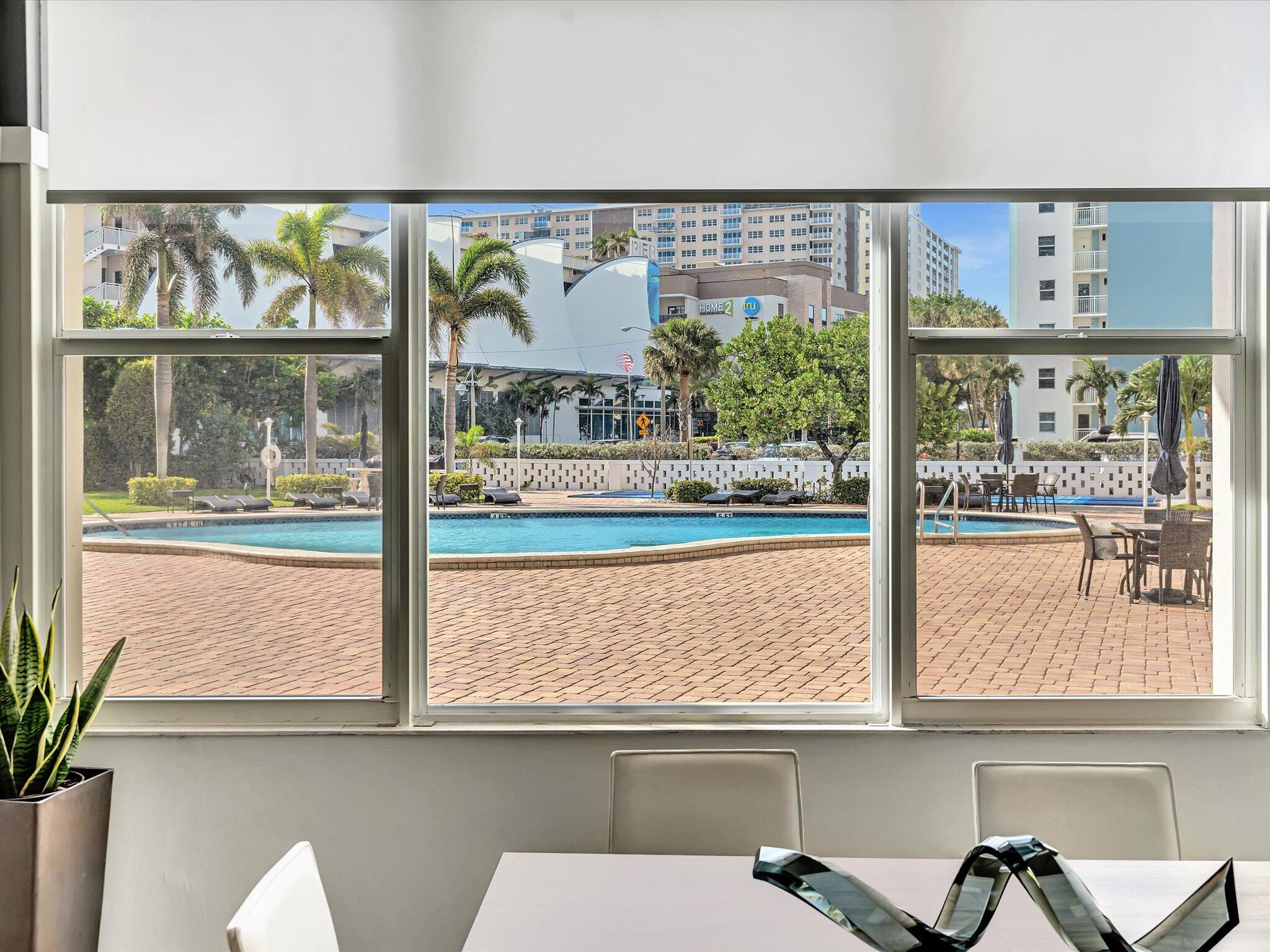 Dining area overlooking a swimming pool and palm-lined deck through a wide window.
