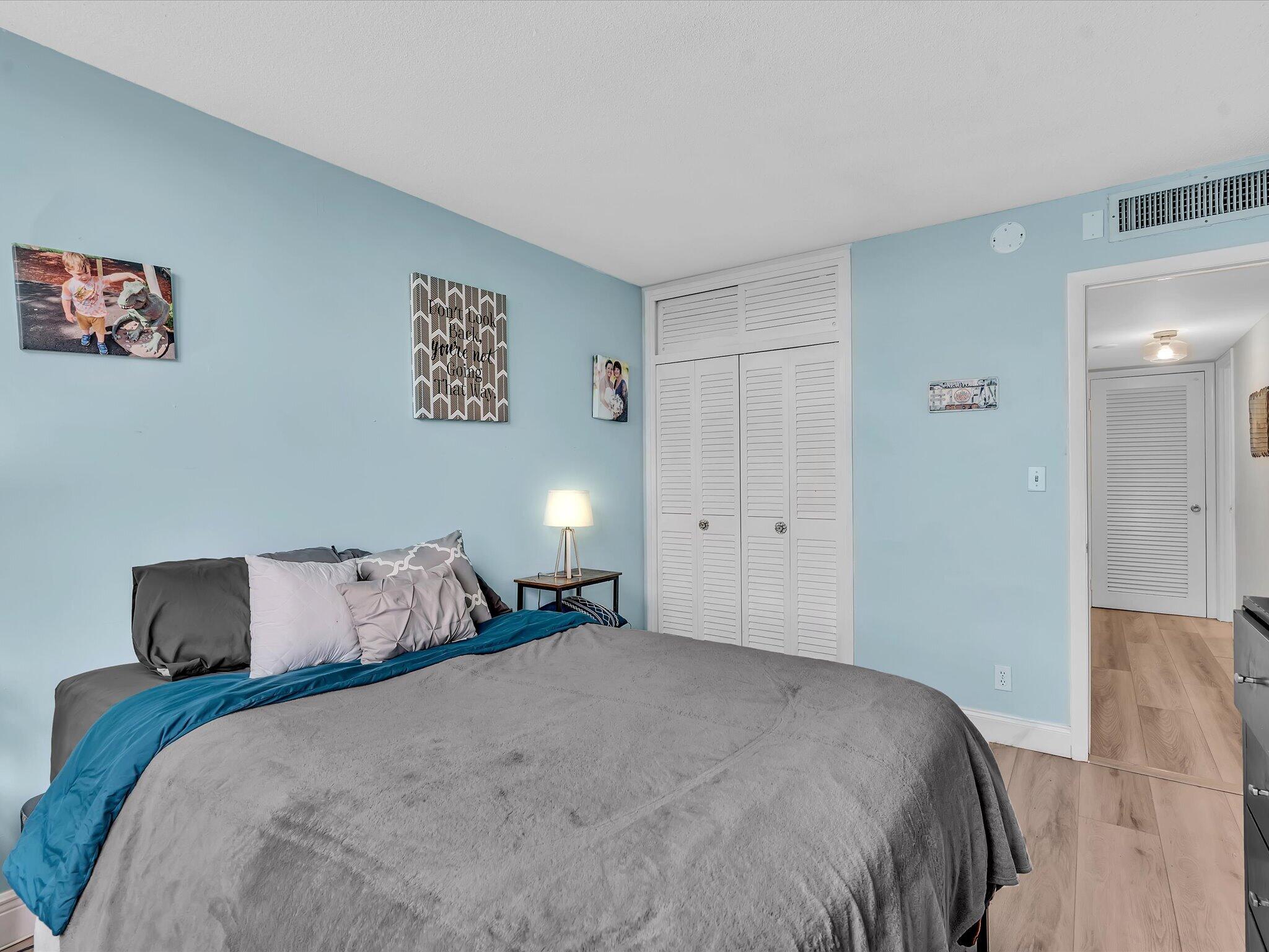 Bedroom with a gray bed and teal blanket, pale blue walls, and white louvered closet doors.