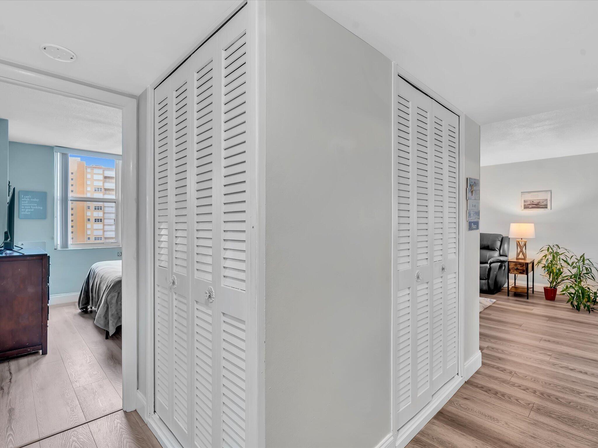 Condo interior with louvered closets separating a blue bedroom from a furnished living area.