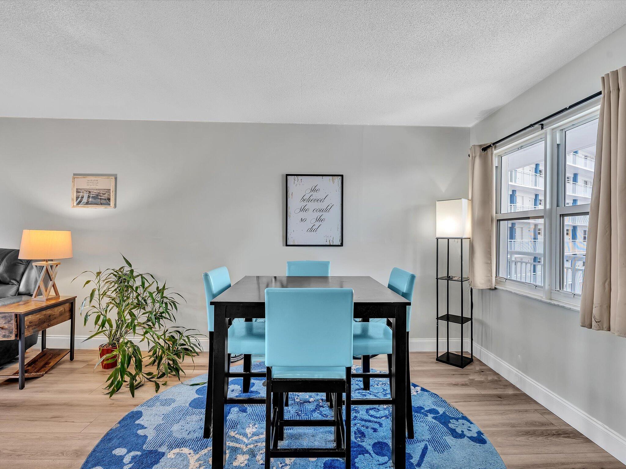 Dining room with turquoise chairs, a black table, blue rug, and large windows.
