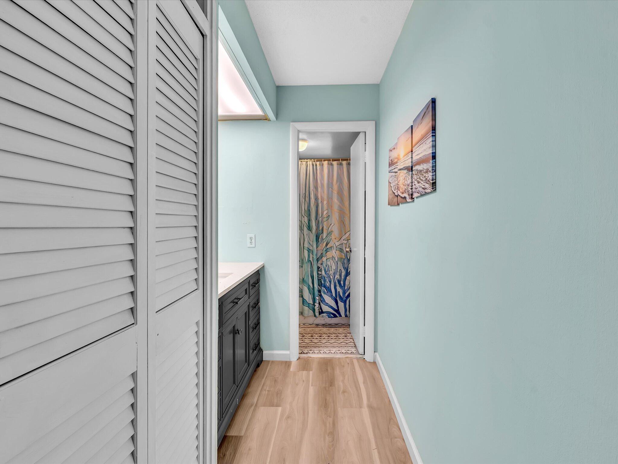 Bathroom with aqua walls, dark vanity, louvered doors, and a colorful botanical shower curtain.