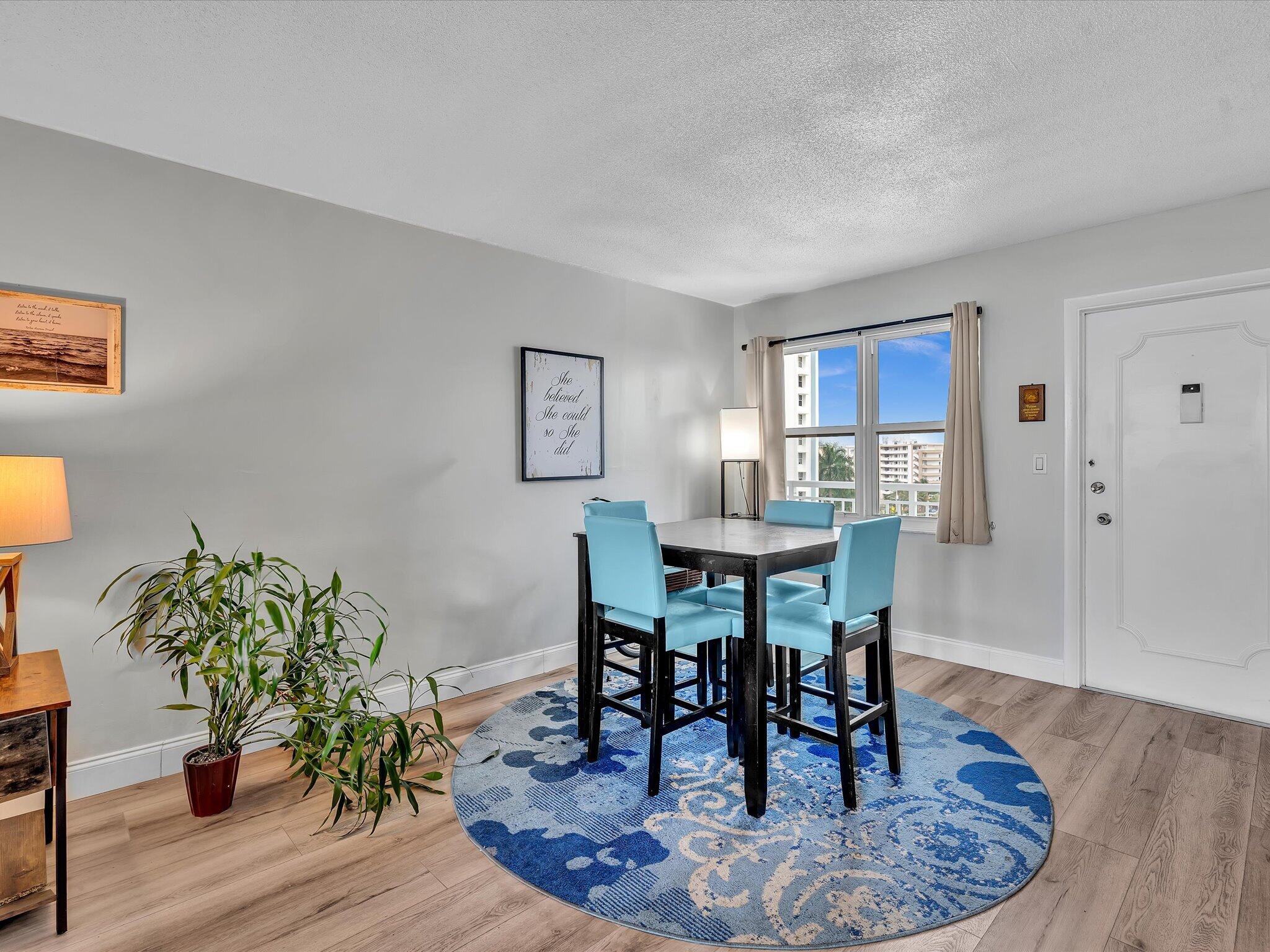 Dining area with turquoise chairs, a blue patterned rug, and a window overlooking nearby buildings.